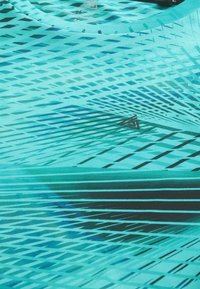 Tela turquesa con un patrón dinámico de líneas diagonales en azul oscuro y negro, con un acabado texturizado y suave, y un diseño de cuello redondo.