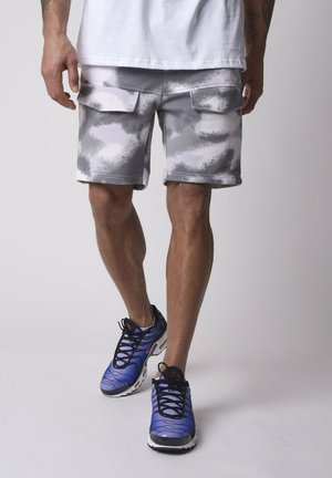 Gray and white tie-dye cargo shorts with two side pockets, paired with blue athletic shoes featuring black laces and white soles.