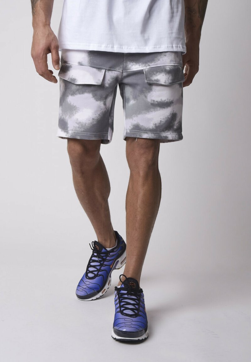 Shorts cargo gris et blanc en tie-dye avec deux poches latérales, associés à des chaussures de sport bleues avec des lacets noirs et des semelles blanches.