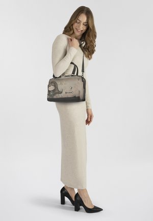 Beige Handtasche mit Grafikdesign, "Annie", und dem Wort "Träume". Schwarze Akzente, glatte Textur, doppelte Griffe und verstellbarer Schultergurt.