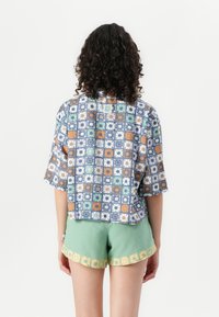 Short-sleeved shirt with a blue geometric floral pattern, paired with mint green shorts featuring a yellow floral hem. Both made from lightweight fabric.