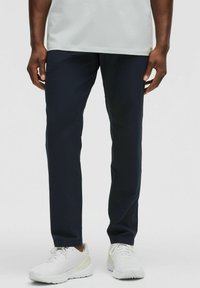 Pantalones deportivos en azul marino con una textura suave y un corte ajustado, combinados con zapatillas blancas. El diseño presenta costuras mínimas y detalles sutiles.