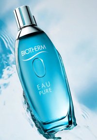La bouteille Biotherm Eau Pure présente un design en verre clair et courbé avec une teinte bleue. Un capuchon argenté, une étiquette avec un texte blanc et un détail circulaire.
