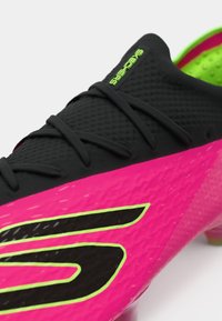 Crne atletske cipele s ružičastim i zelenim potplatom. Imaju teksturiranu površinu, crne vezice i istaknuti crni logo s limeta zelenim detaljima.