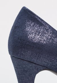 Zapato de tacón alto en color navy con una superficie texturizada y un brillo sutil, diseño de punta afilada y tacón estrecho.