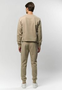 Hanorac bej și pantaloni jogger asortați, confecționați dintr-un material moale; au manșete cu rigole și o croială lejeră. Adidașii albi completează ținuta.