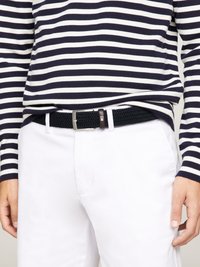 Schwarzer gewebter Gürtel mit einer silbernen Metallschnalle, getragen über weißen Hosen, kombiniert mit einem navy-blauen und weißen gestreiften Langarmhemd.