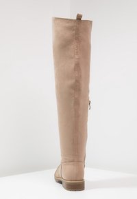 Bota de imitación de cuero beige hasta la rodilla, con una textura suave, costura trasera simple, tira para facilitar el calzado y un tacón redondo bajo. Detalle de cremallera en el lateral.