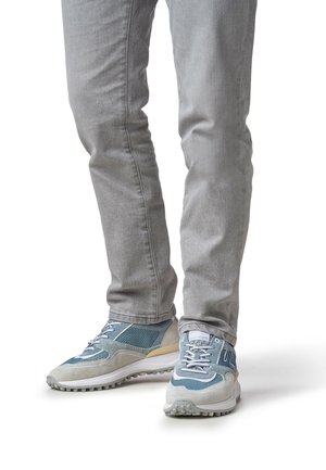 Des baskets bleues et grises avec une tige en mesh et en daim, des lacets blancs et une semelle en caoutchouc texturée. Associées à un jean slim gris clair.