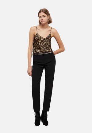 Leren satijnen camisole met luipaardprint en dunne bandjes, gecombineerd met een strakke zwarte broek met een ronde gesp met studs en zwarte enkellaarzen.