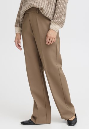 Beige wijde broek gedragen met zwarte platte schoenen en een grofgebreide trui in neutrale tinten, zichtbaar van taille tot voeten.