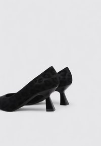 Chaussures à talons hauts imprimées léopard noires avec un bout rond et un design de talon angulaire unique, fabriquées en tissu texturé.