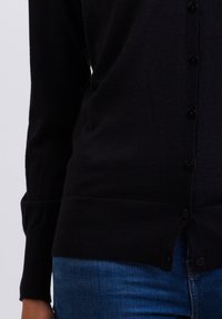 Černý pletený cardigan s přiléhavým střihem, dlouhými rukávy, kulatým výstřihem a knoflíky na přední straně. Měkká textura, viditelné švy.