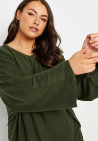 Grön oversized fleece-tröja med vida ärmar och rund halsringning. Mjuk textur, avslappnad design och minimala sömnadsdetaljer.