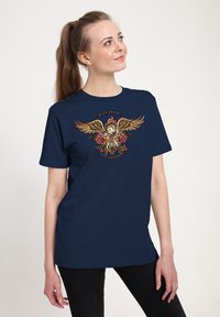 Navyblaue Kurzarm-T-Shirt mit einem detaillierten Grafik eines geflügelten Wesens mit einem Schädel und floralen Akzenten. Glatte Stofftextur.