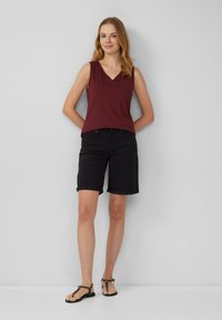 Bordeaux mouwloze top met V-hals, gecombineerd met zwarte opgerolde shorts en platte sandaal. Eenvoudig ontwerp, getailleerde silhouet, lichtgewicht stof.