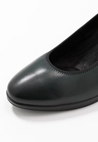 Close-up of black leather flat shoe with rounded toe and elastic trim on white background.