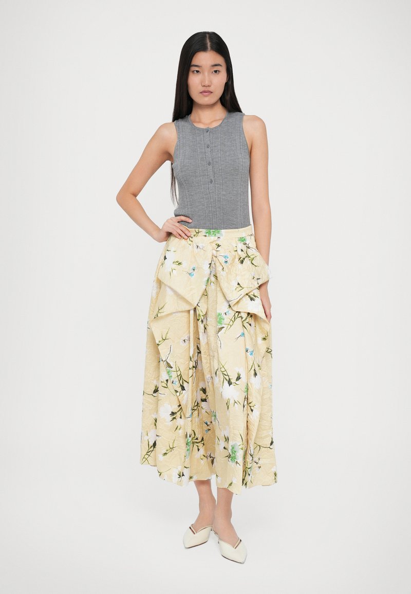 Graues, geripptes, ärmelloses Oberteil mit Knopfdetails, kombiniert mit einem gelben Rock mit floralen Mustern, der im Lagenlook und knielang ist.