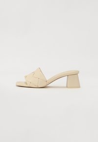 Beige high-heeled sandal with a woven leather upper, square toe, and a chunky triangular heel. Smooth texture with minimal detailing.