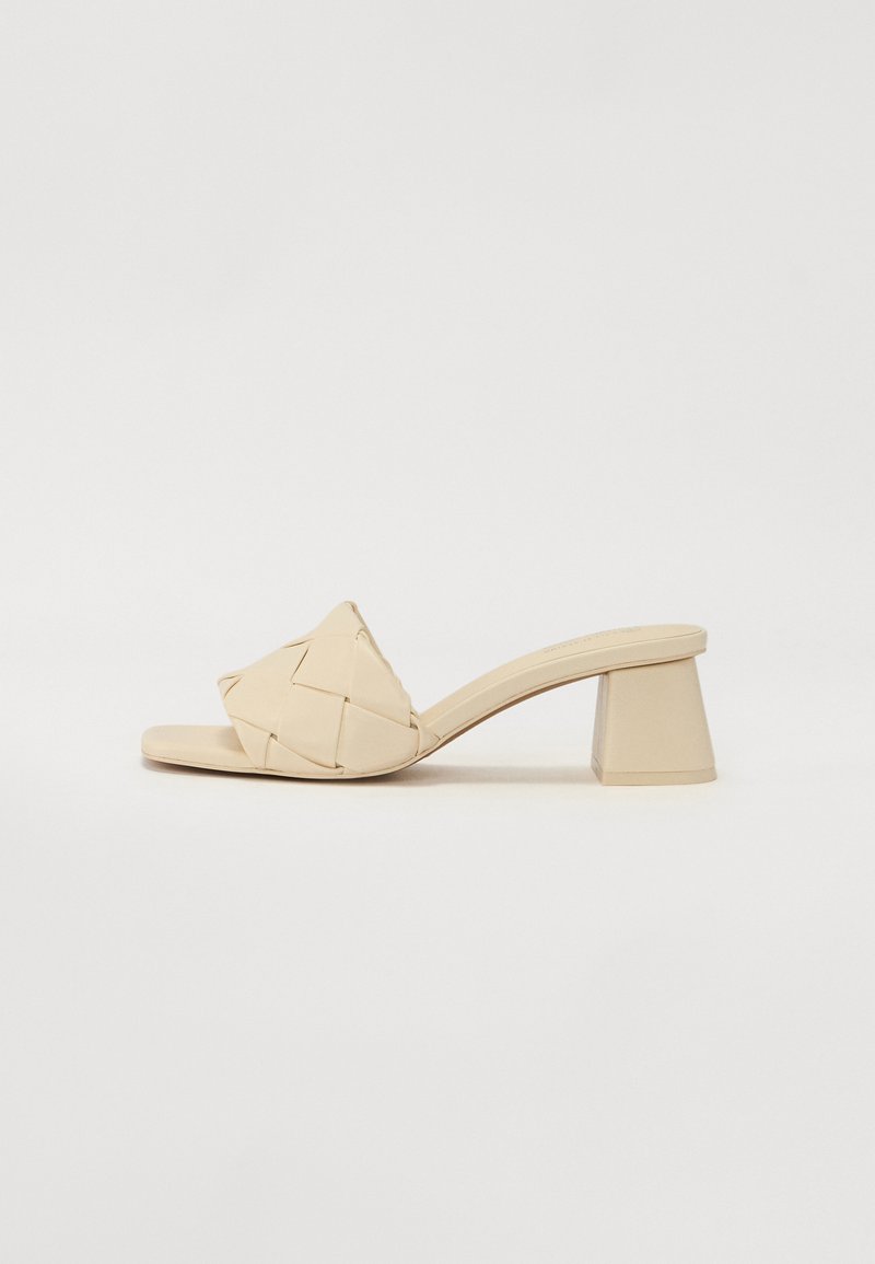 Beige high-heeled sandal with a woven leather upper, square toe, and a chunky triangular heel. Smooth texture with minimal detailing.