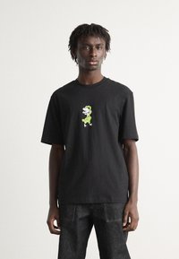 Camiseta negra de algodón con un gráfico central de un personaje de dibujos animados en verde. La camiseta tiene cuello redondo y mangas cortas, con un corte relajado.