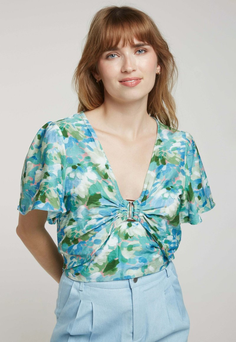 Haut floral avec un décolleté en V, des manches courtes en volants et un détail torsadé au centre, avec des nuances de bleu, vert et rose clair.