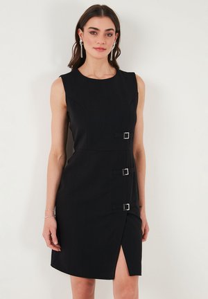 Black sleeveless dress featuring a fitted silhouette, side slit, and three rectangular silver buckle accents on the waist. Smooth fabric texture.