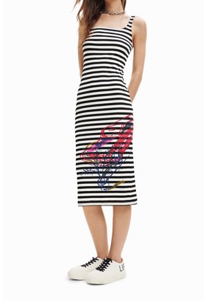 Femme portant une robe midi sans manches à rayures noires et blanches avec un graphique de voiture coloré et des baskets blanches à lacets noirs.