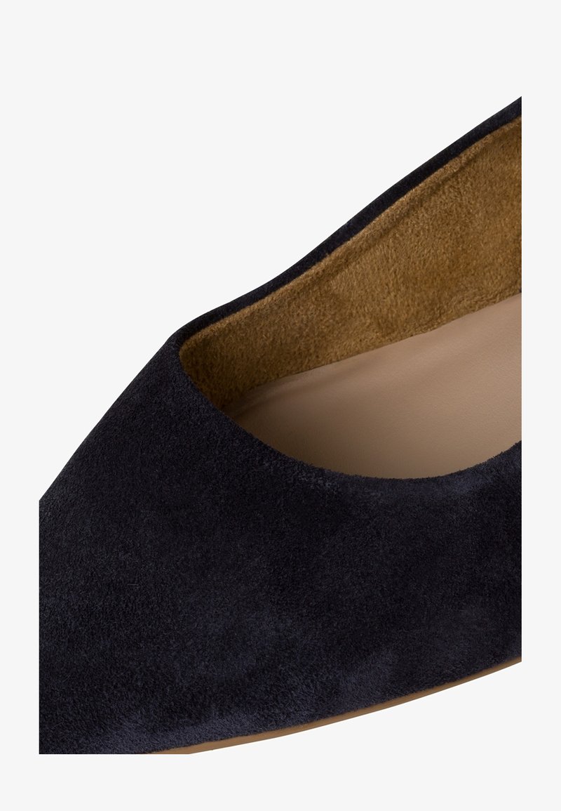 Gros plan sur une chaussure plate en daim bleu nuit avec un bout arrondi et une doublure intérieure en cuir beige.