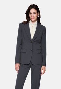 Gray suit jacket with a single-breasted design, two front pockets, black buttons, and tailored silhouette, paired with a cream blouse.