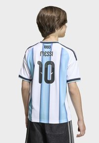 Enfant tourné le dos portant un maillot de football de l'Argentine avec des rayures bleues et blanches, le numéro 10, et le nom "Messi" au dos.