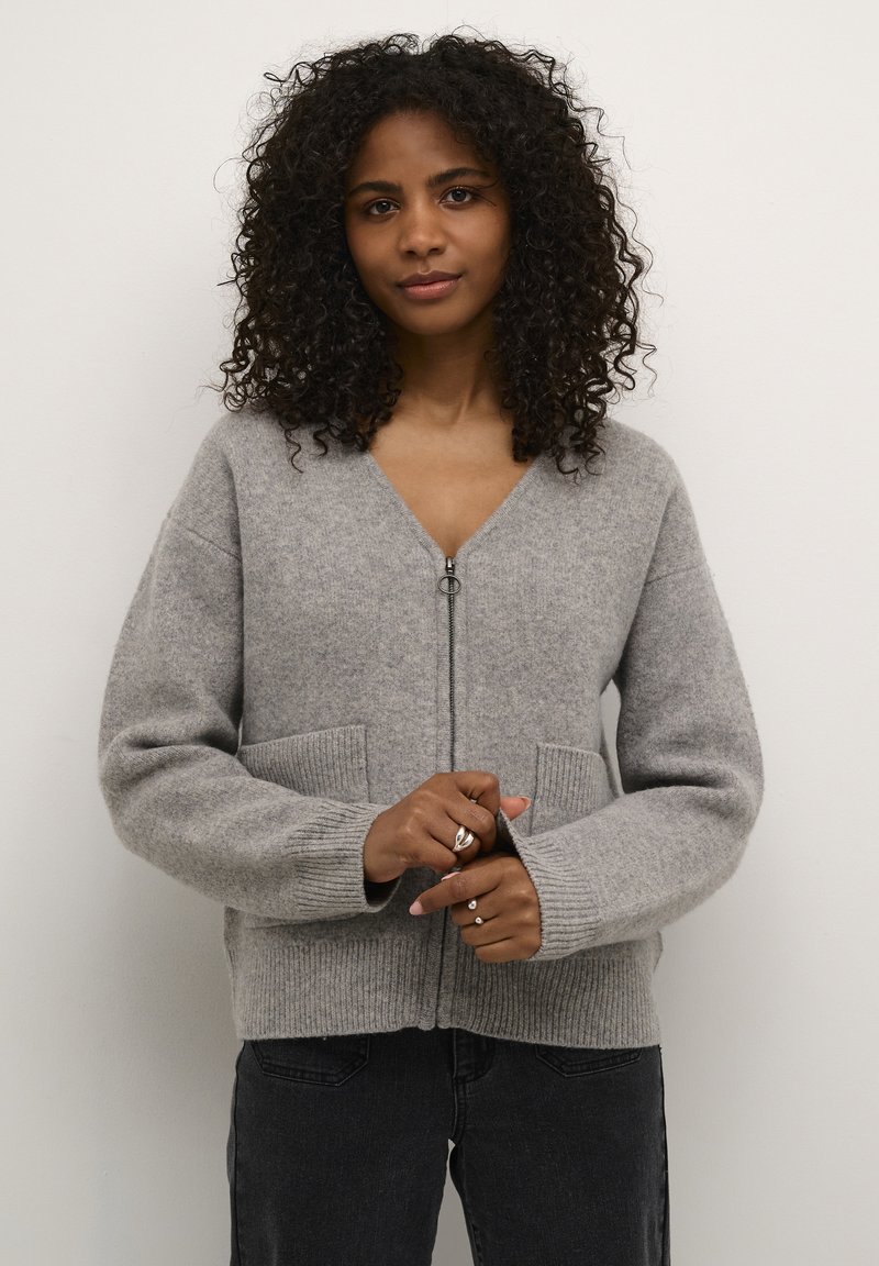Helle graue Strickjacke mit V-Ausschnitt und Reißverschluss vorne. Verfügt über zwei Fronttaschen und gerippte Bündchen. Weicher Stoff, lässiges Design.