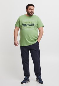 Groen katoenen T-shirt met de opdruk "Blend Denim Original Vintage" in marineblauw, gecombineerd met marineblauwe broek met elastische taille en donkere sneakers.