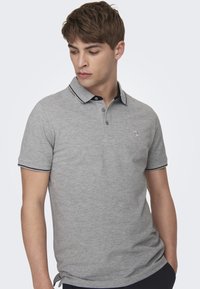 Graues Poloshirt mit kurzen Ärmeln, schwarzem Kragen und kontrastierenden Details. Verfügt über ein Logo auf der linken Brust und einen strukturierten Stoff.