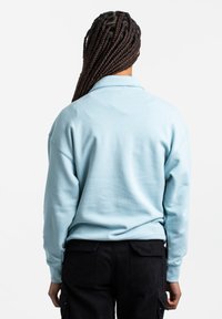 Sudadera azul clara con cuello tipo polo, corte relajado y puños acanalados, combinada con pantalones cargo negros que tienen bolsillos laterales.