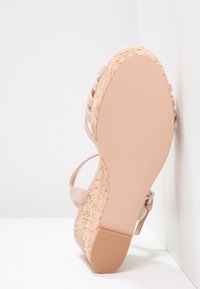 Sandale compensée avec tige synthétique rose clair ornée de brides horizontales, talon en liège texturé et semelle beige lisse.