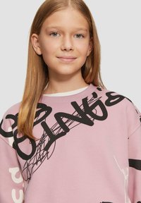 Light pink oversized sweatshirt made of soft fabric, featuring bold black graphic designs and text. Round neck and long sleeves.