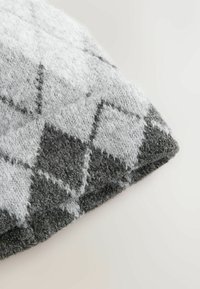 Grau-weißes Gewebe im Argyll-Muster mit einer weichen, strukturierten Oberfläche, das eine umgeschlagene Ecke und kontrastierende dunkelgraue Akzente aufweist.