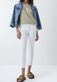 Džínová bunda s vyhrnutými rukávy, olivově zelené tričko, bílé úzké džíny a hnědé sandály s mašlí.