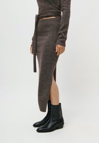 Jupe en tricot marron avec un design enroulé, dotée d'une fente latérale et d'une ceinture à nouer, associée à des bottines noires.