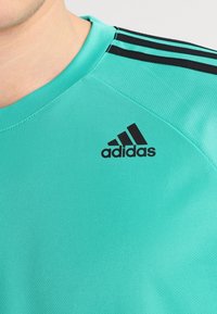 Turquoise athletic t-shirt with a round neck, made of textured fabric, featuring black three-stripe accents and an adidas logo on the chest.