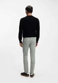 Czarny sweter z teksturą, jasnoszare spodnie slim-fit i czarne trampki z białymi akcentami, widok z tyłu na białym tle.