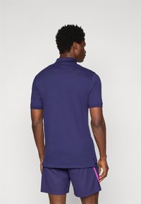 Navy polo shirt with short sleeves, made of smooth fabric. Features a classic collar and a side split hem, paired with textured shorts.
