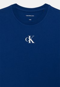Zila kokvilnas t-kreklu ar apaļu dekoltē. Uz krūtīm ir balts "ck" logo. Gluda tekstūra ar ikdienišķu dizainu.