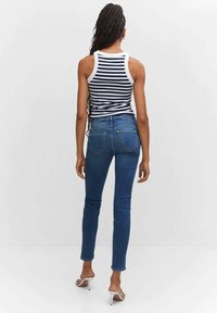 Blue denim skinny jeans with a mid-rise, featuring a classic five-pocket design and a smooth texture. Paired with a striped sleeveless top.