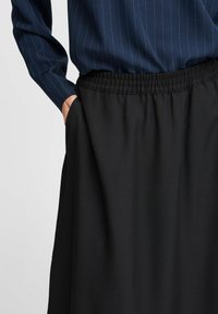Jupe noire avec une taille élastique, présentant une texture lisse et des poches latérales. Accompagnée d'une chemise à rayures bleu marine à manches longues.