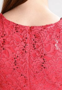 Robe en dentelle rouge avec des sequins, dotée d'une fermeture éclair au dos et d'un motif floral ; la texture semble délicate et complexe.