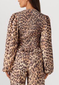 Leopard print blouse with puffed sleeves. Features smocked back and ruffled hem. Material is lightweight with a silky texture in beige and brown tones.