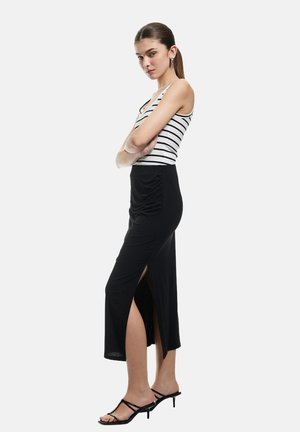 Gonna maxi nera con spacco laterale e tessuto arricciato, abbinata a una canotta bianca a righe. Modella che indossa sandali neri con cinturino.