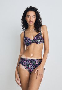 Floral patterned bikini set featuring a black background with vibrant purple, pink, and green leaves. The top has a structured design, adjustable straps, and the bottoms have side ties.